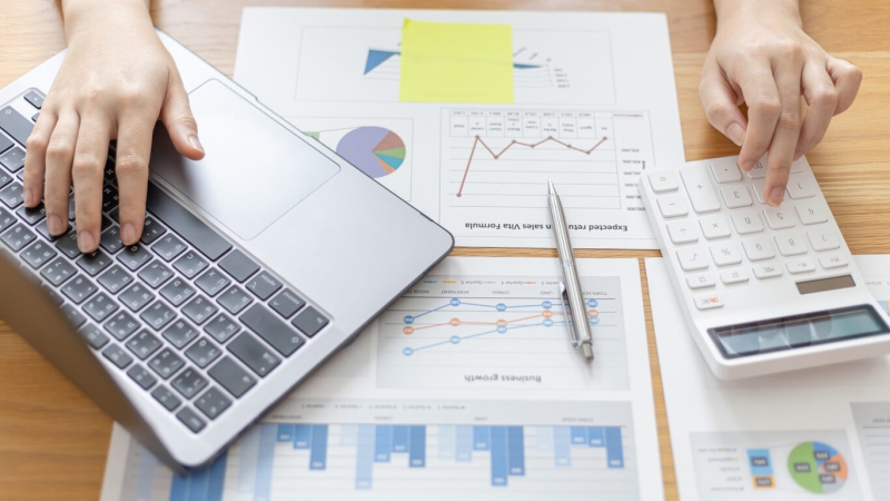 person using laptop and calculator to examine revenue data